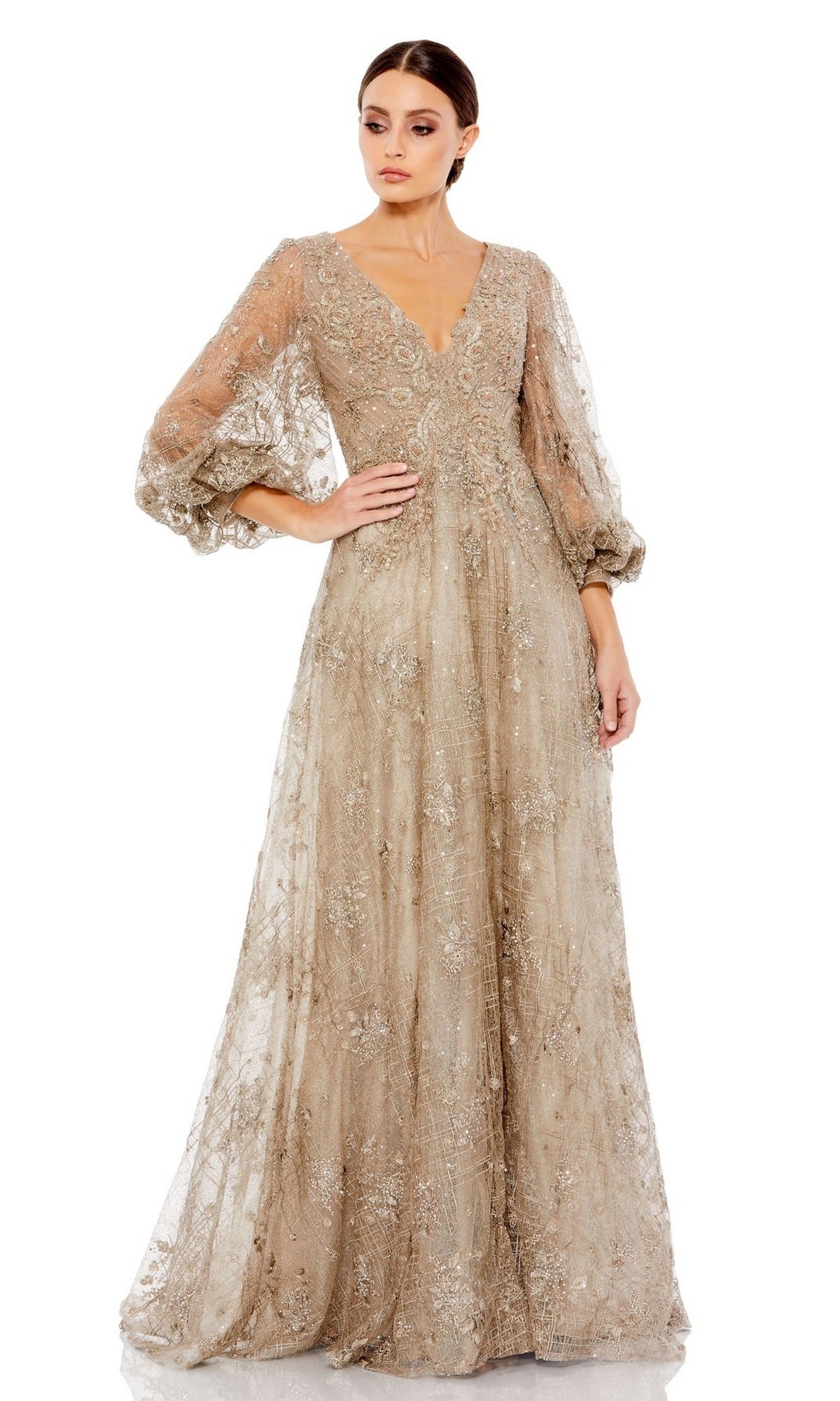 A woman wears the Long Formal Dress 20283 by Mac Duggal, featuring sheer puff sleeves, intricate embroidery, and a gold A-line silhouette, standing against a plain white background.